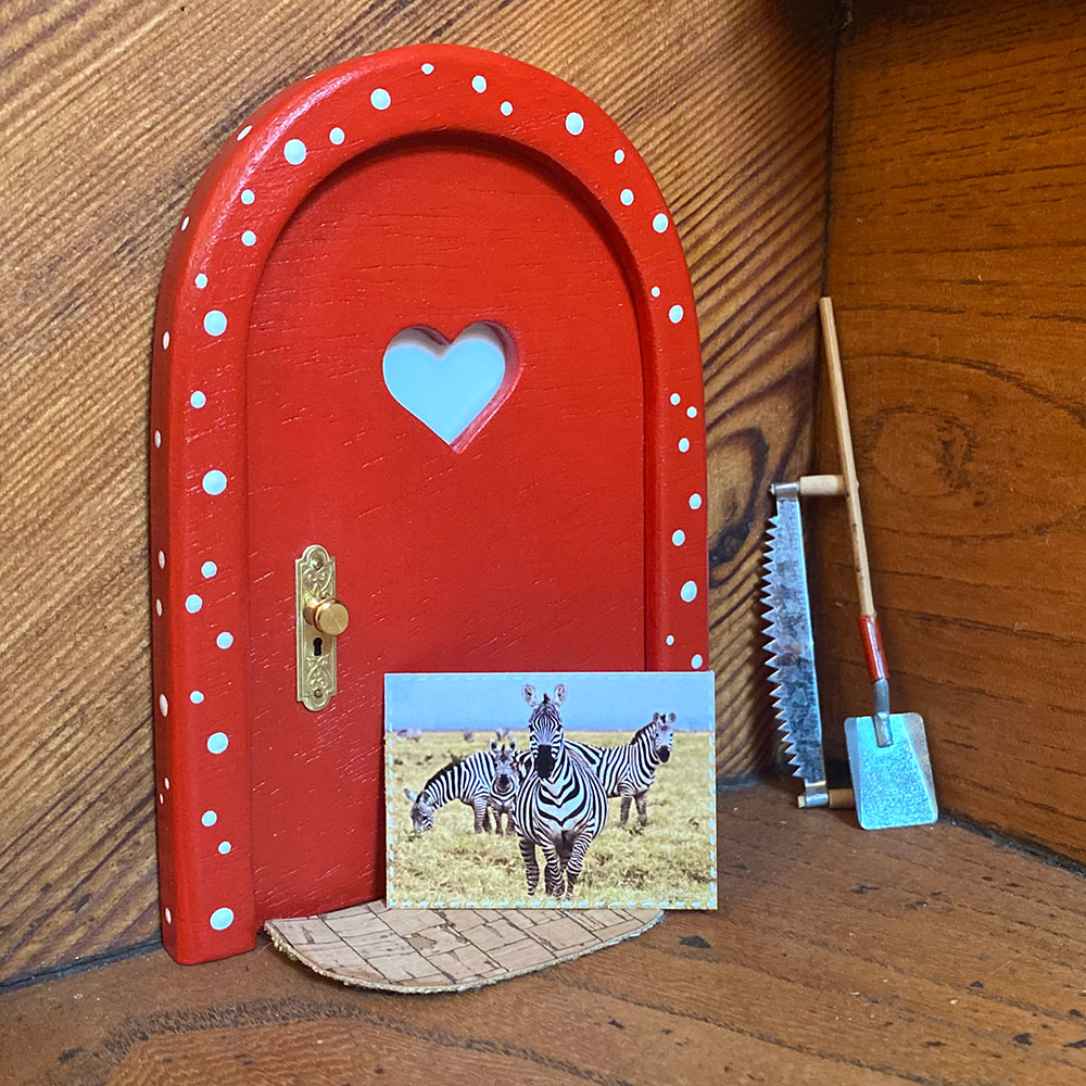 Kleine Postkarte mit einem Zebra vor einer roten Wichteltür